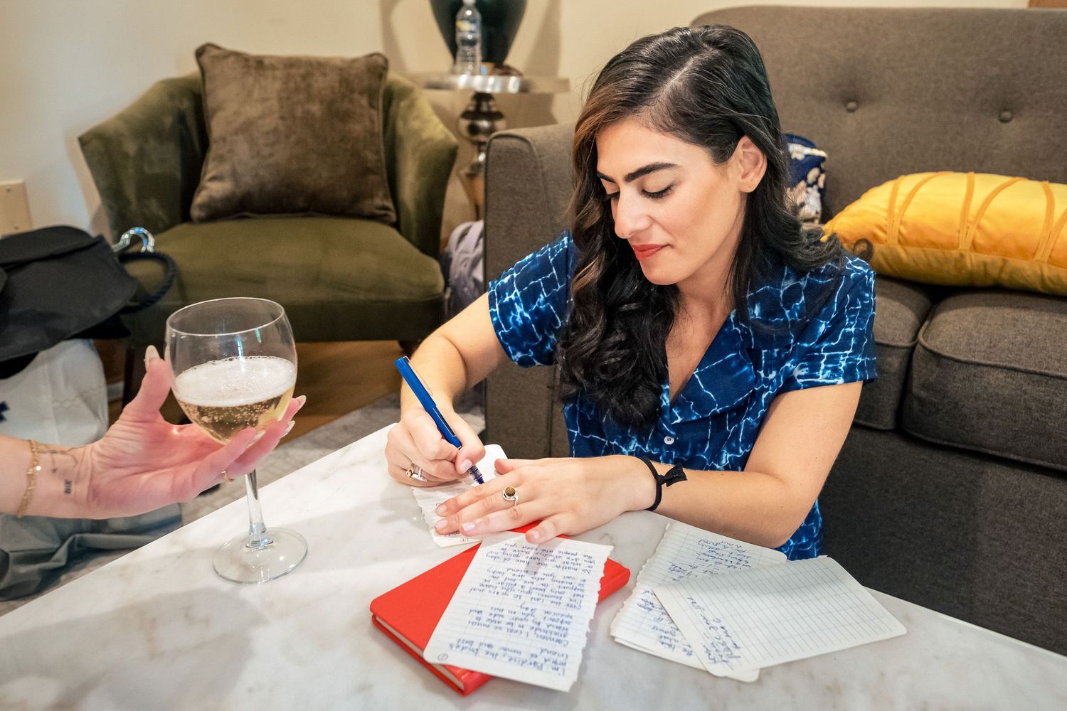 Bride in blue dress writes wedding vows at a table with a glass of white wine nearby.