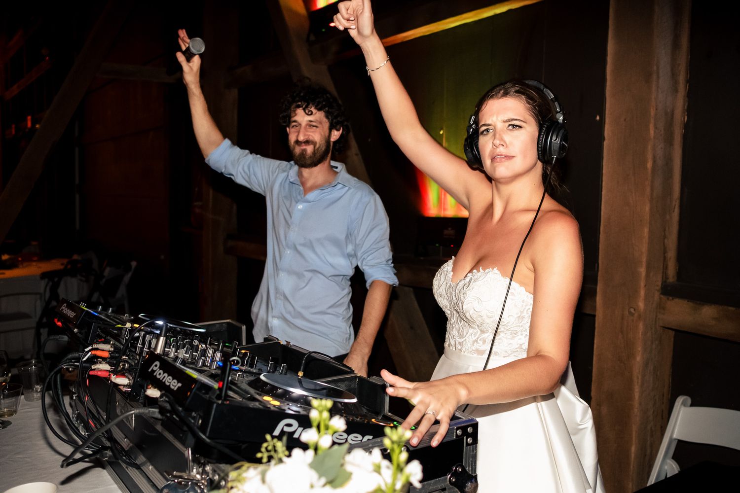 Bride and groom celebrating at DJ booth with hands raised at their wedding reception.