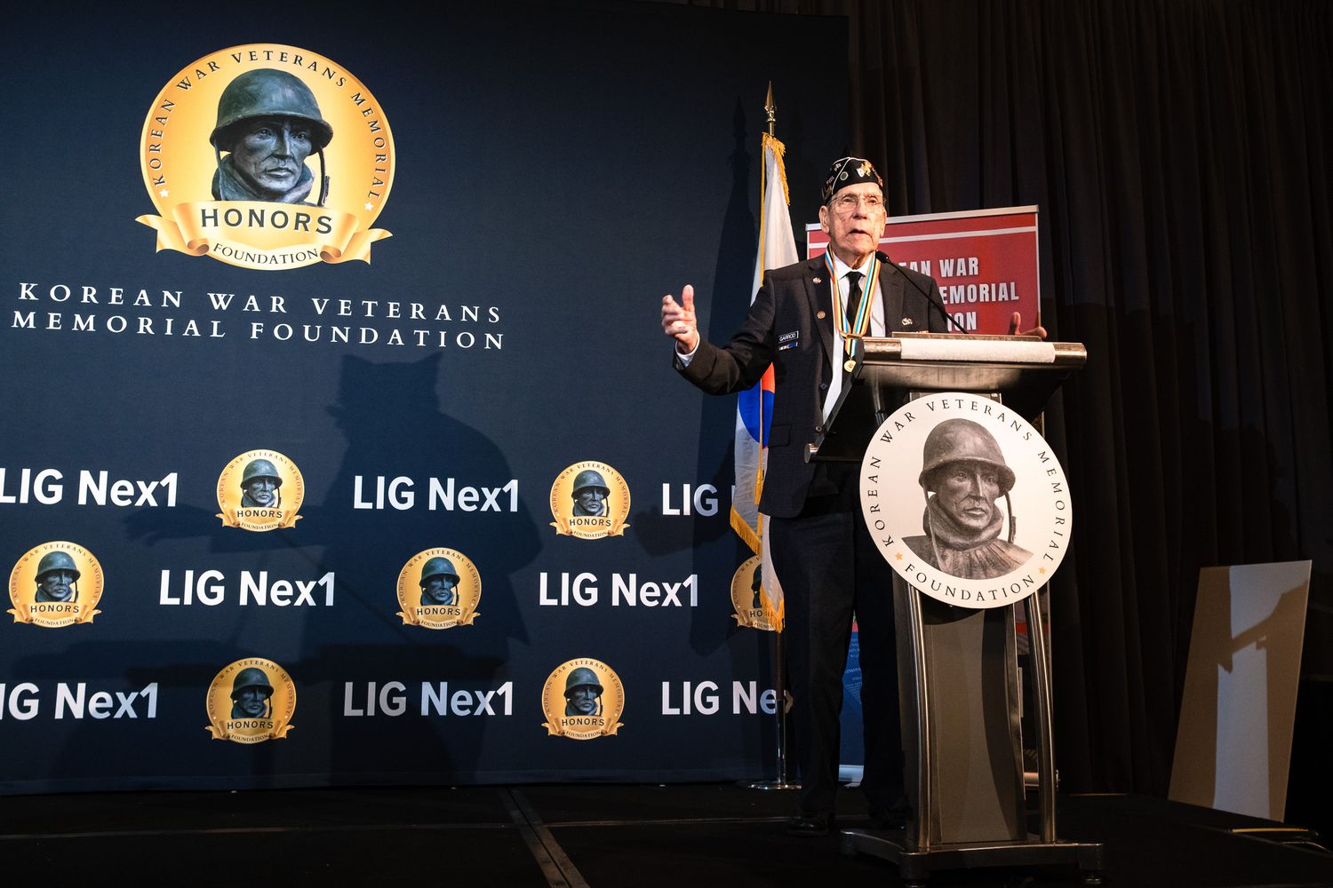 Veteran speaks at Korean War Veterans Memorial Foundation honors event at LIG Nex1 sponsored podium.