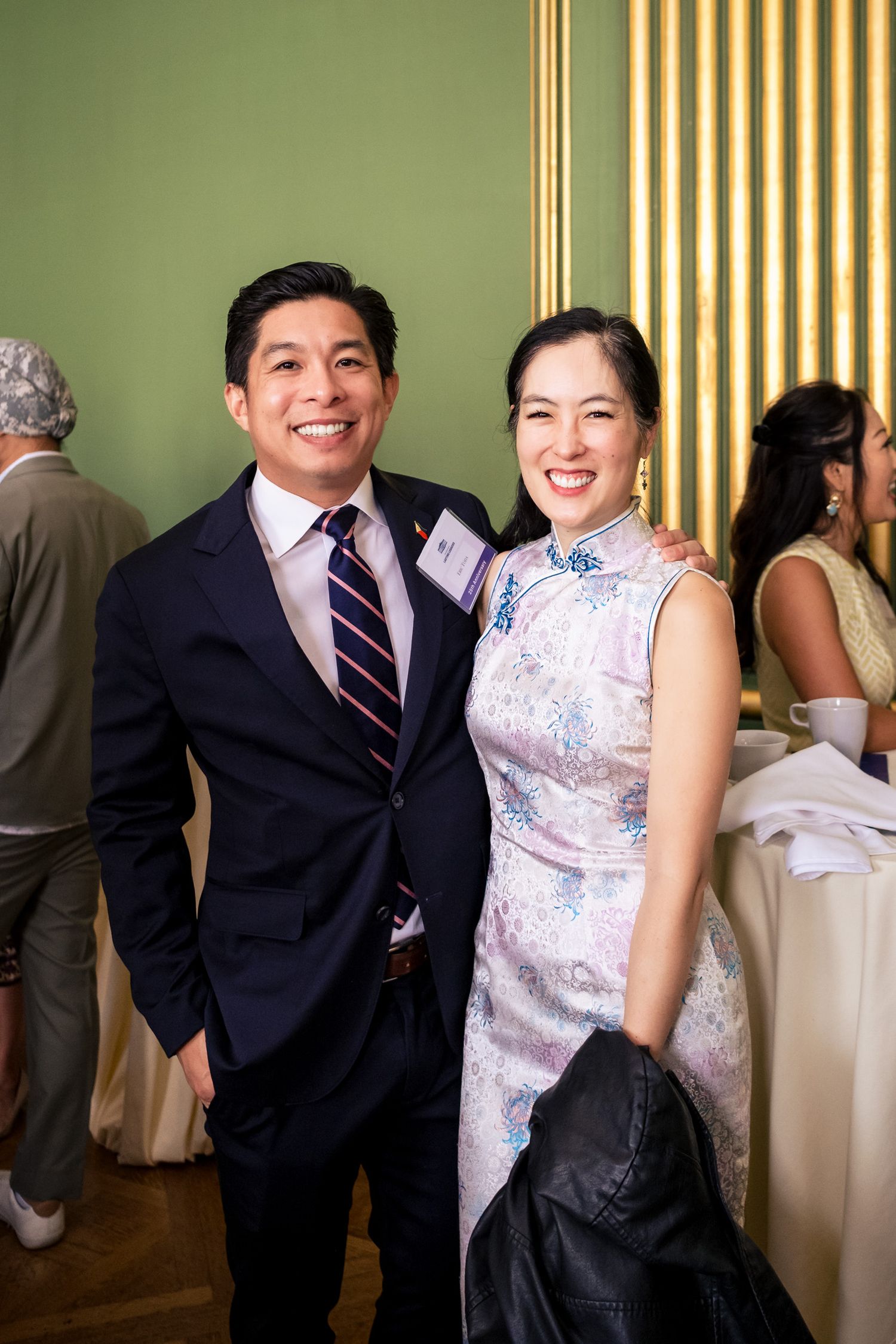 A smiling man in a suit and woman in a floral qipao pose together at an elegant formal event.