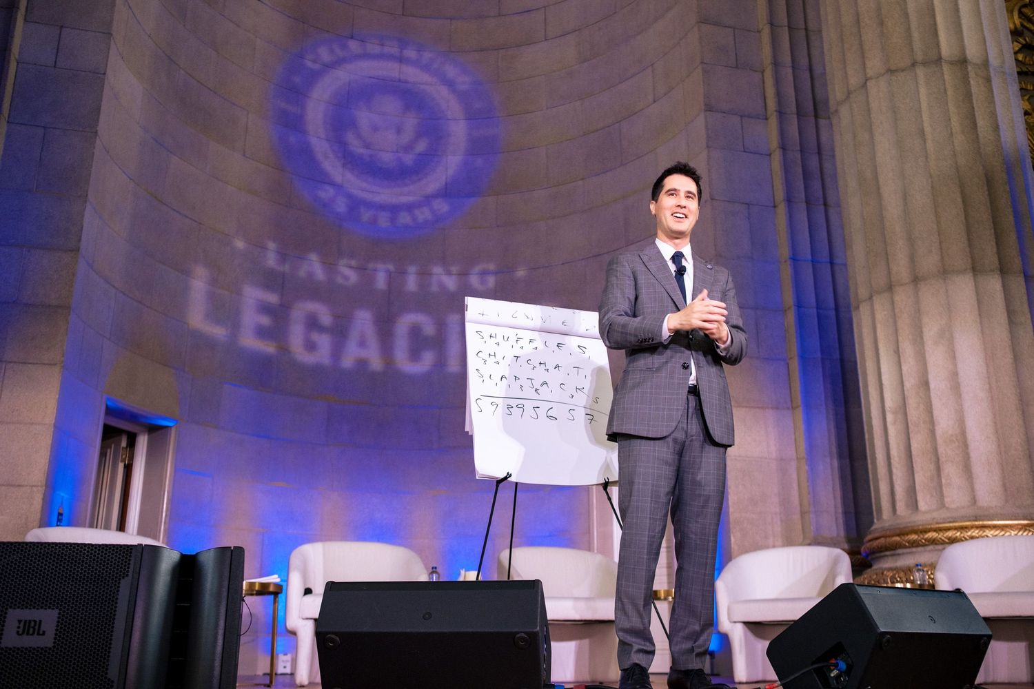 Speaker presenting at Lasting Legacy 75 Years gala event in elegant venue with blue lighting.