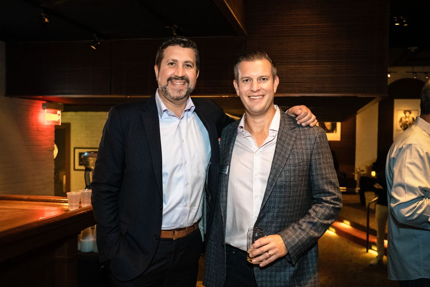 Two men in blazers smile together at an upscale restaurant event.