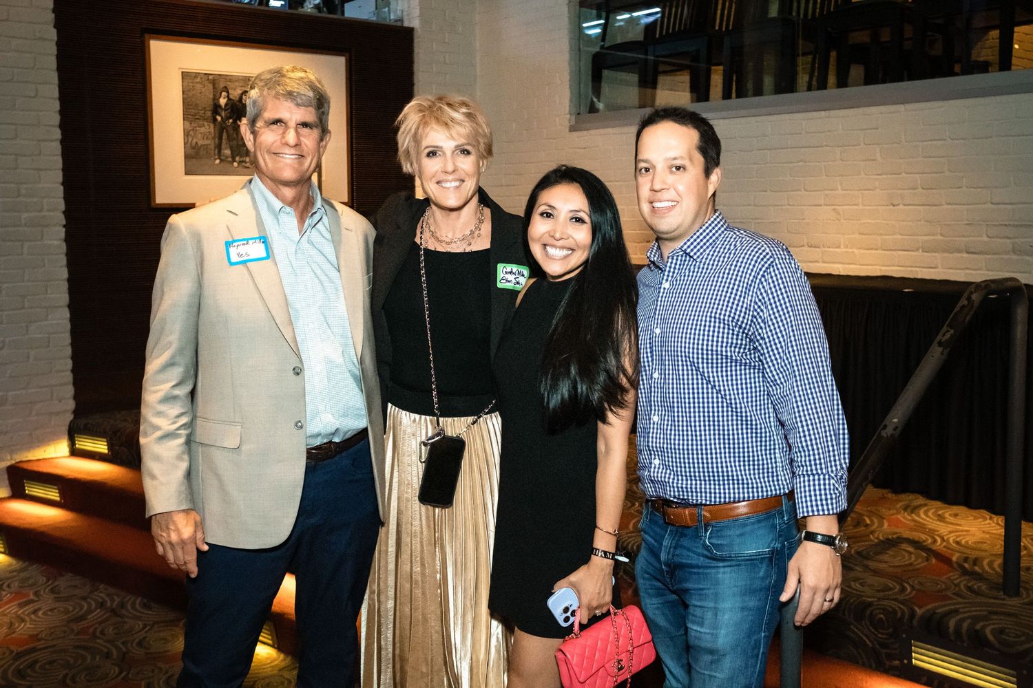 Four guests smile together at an indoor social event, dressed in smart casual attire.