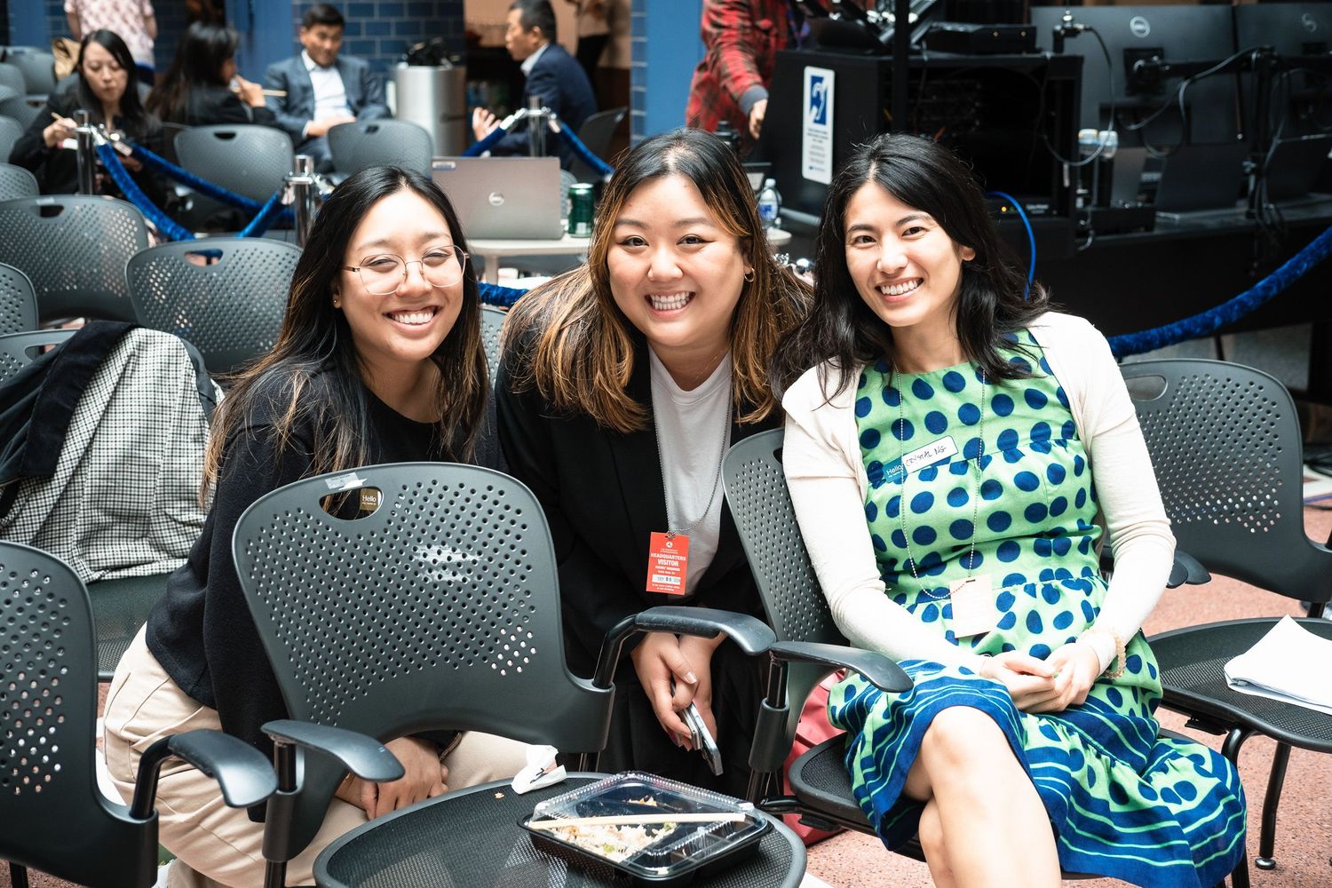 Three smiling women pose together at a professional conference event seated in chairs.