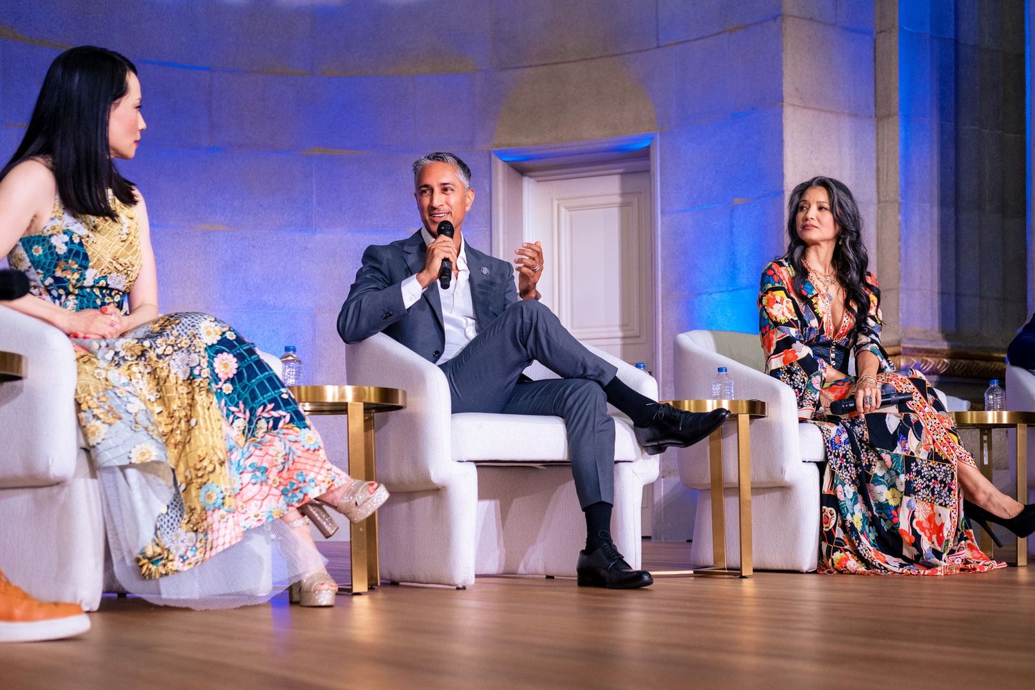 Three panelists in colorful attire seated on white chairs during an elegant conference or event discussion.