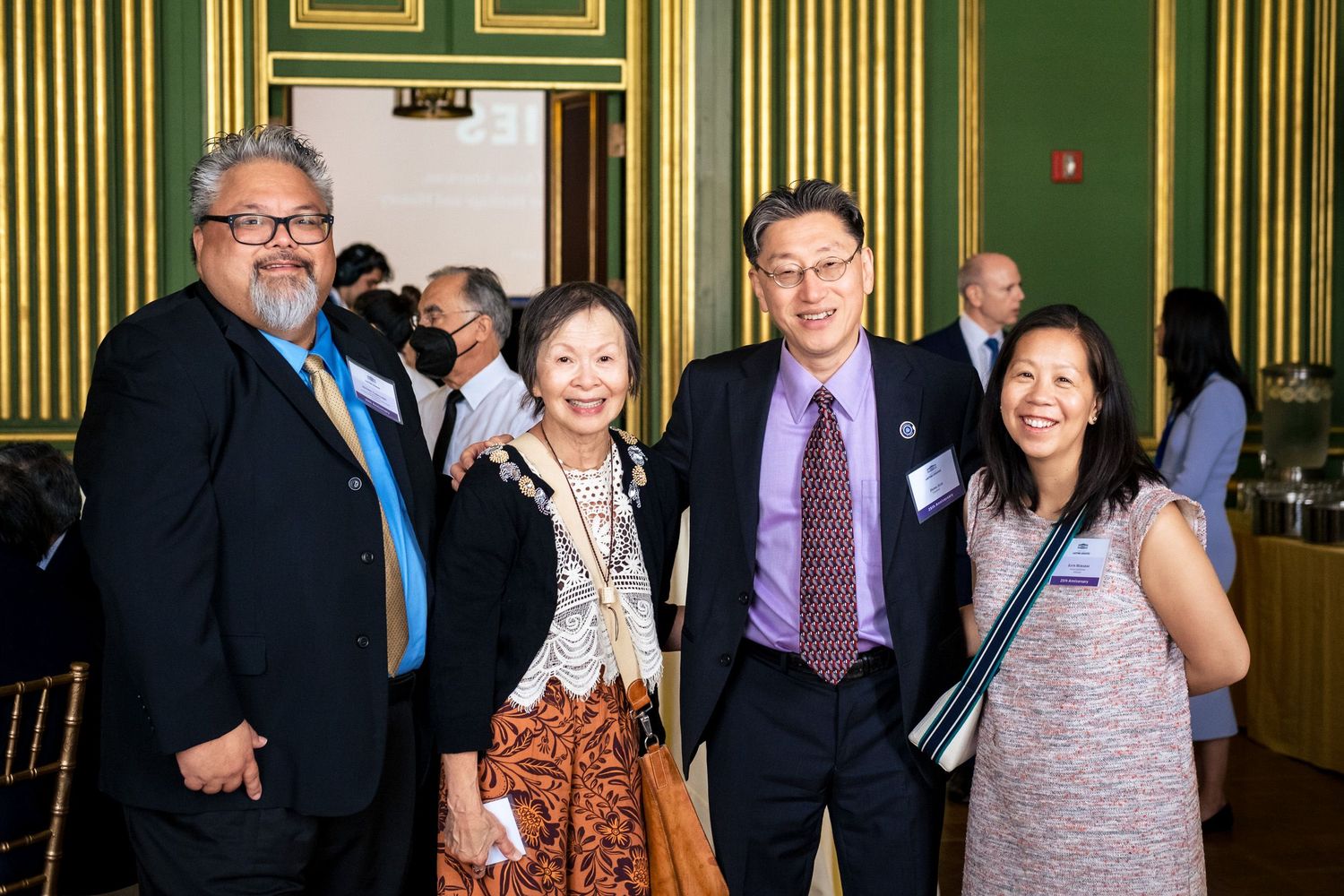 Four professionals smiling together at a formal networking event in an elegant green-walled venue.