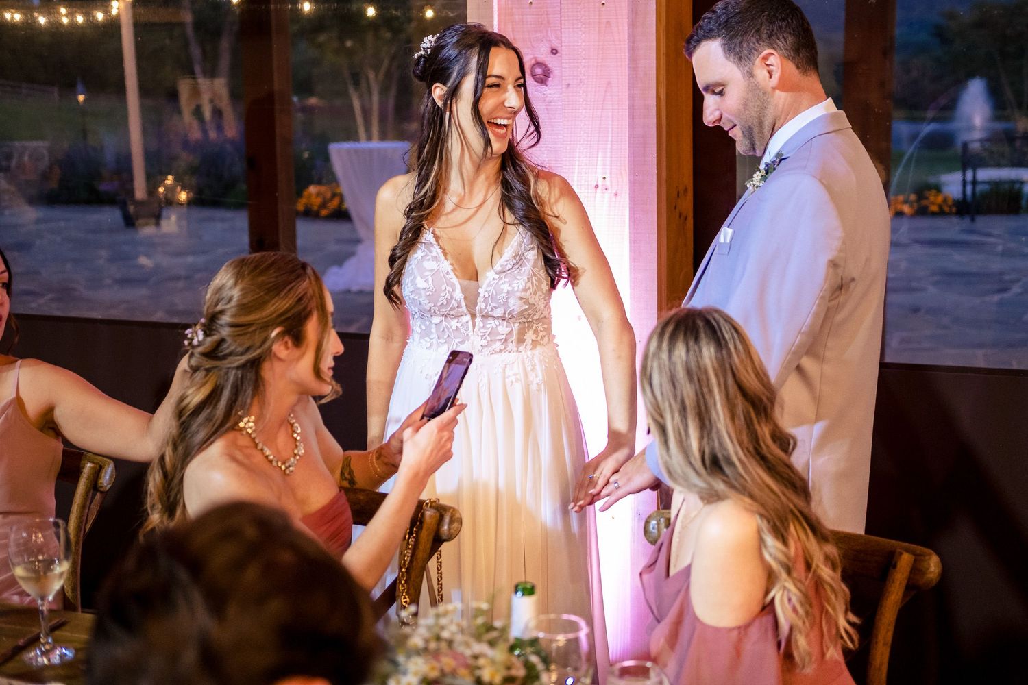 Bride laughing with guests at wedding reception dinner table, wearing white gown.