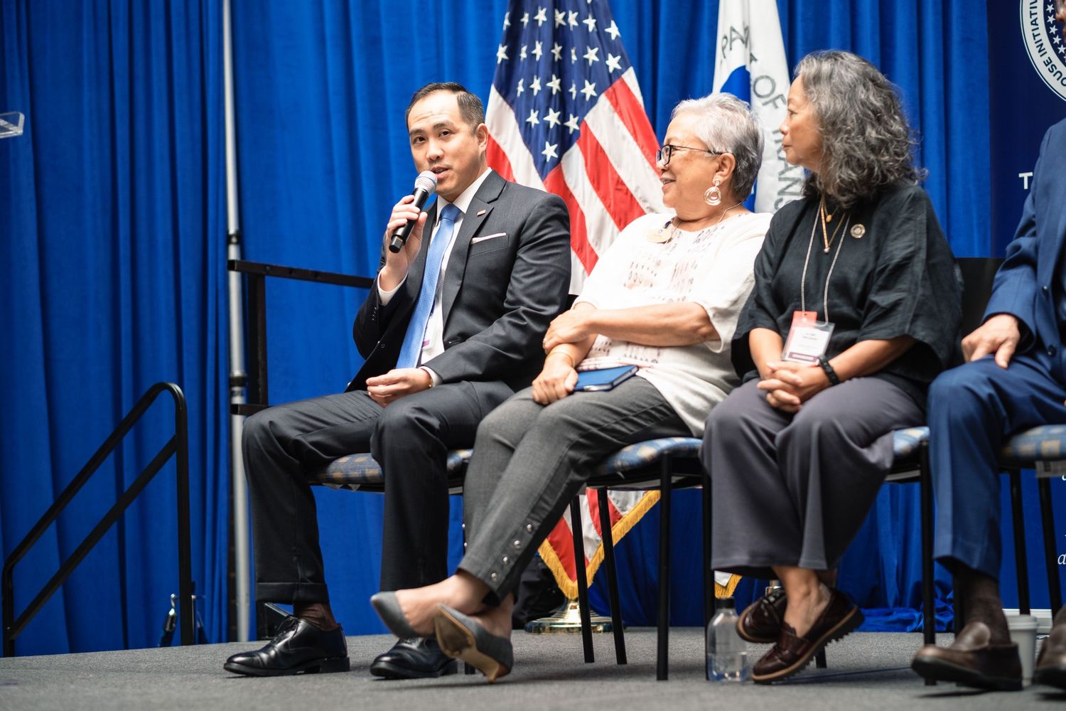 Panel discussion with three speakers seated before American flag at official government event.