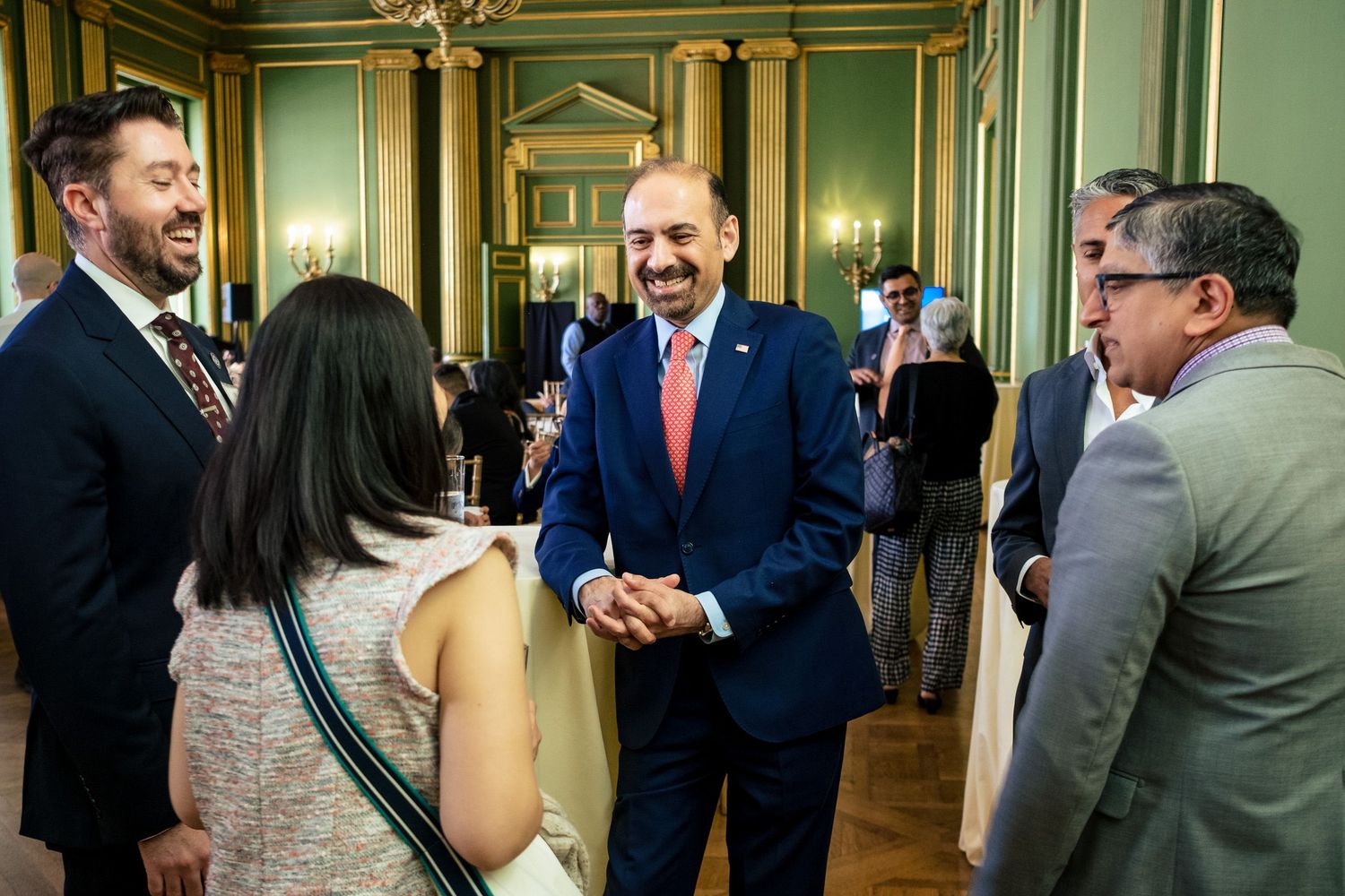 Business professionals networking and laughing together in an elegant green-walled reception hall during a formal event.