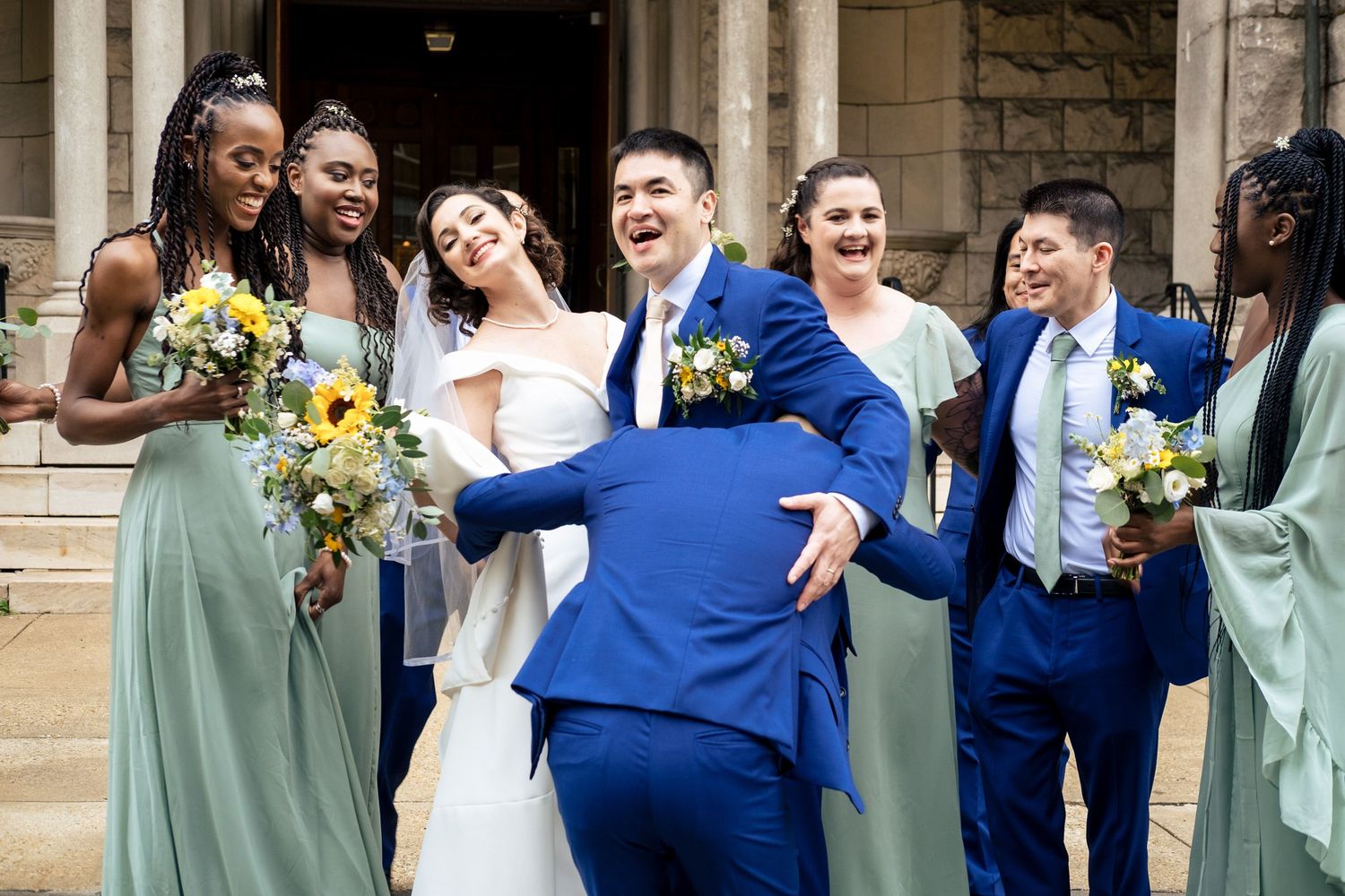 Wedding party laughs and celebrates together outside a stone church after the ceremony.