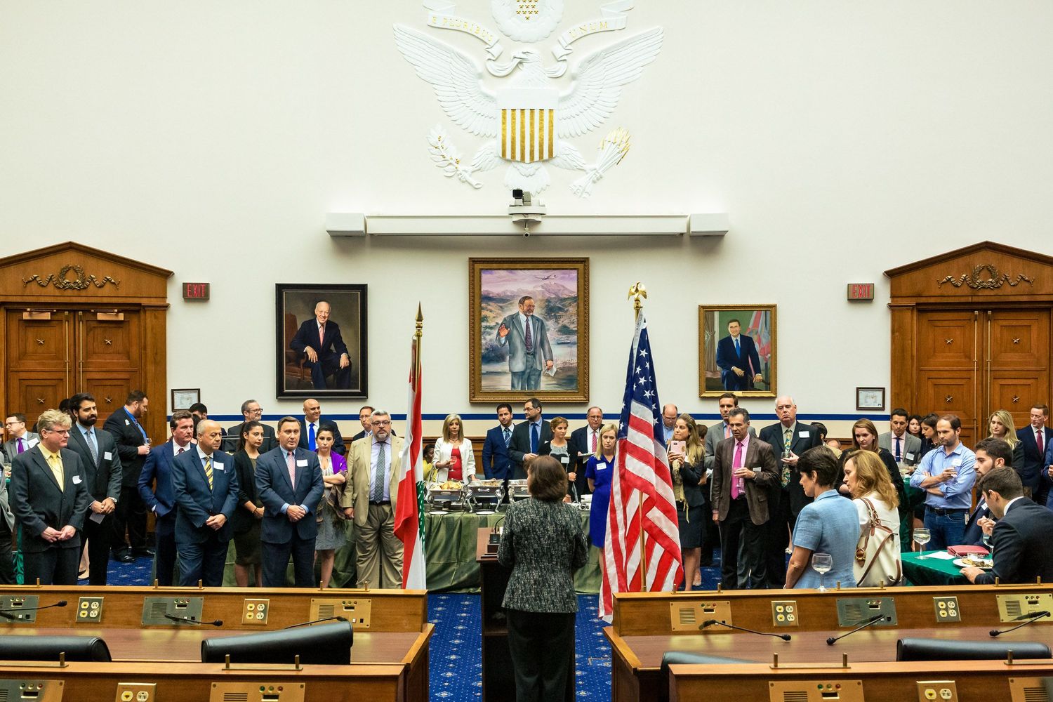 Group of officials standing in a formal U.S. Congressional hearing room with American flags and portraits.
