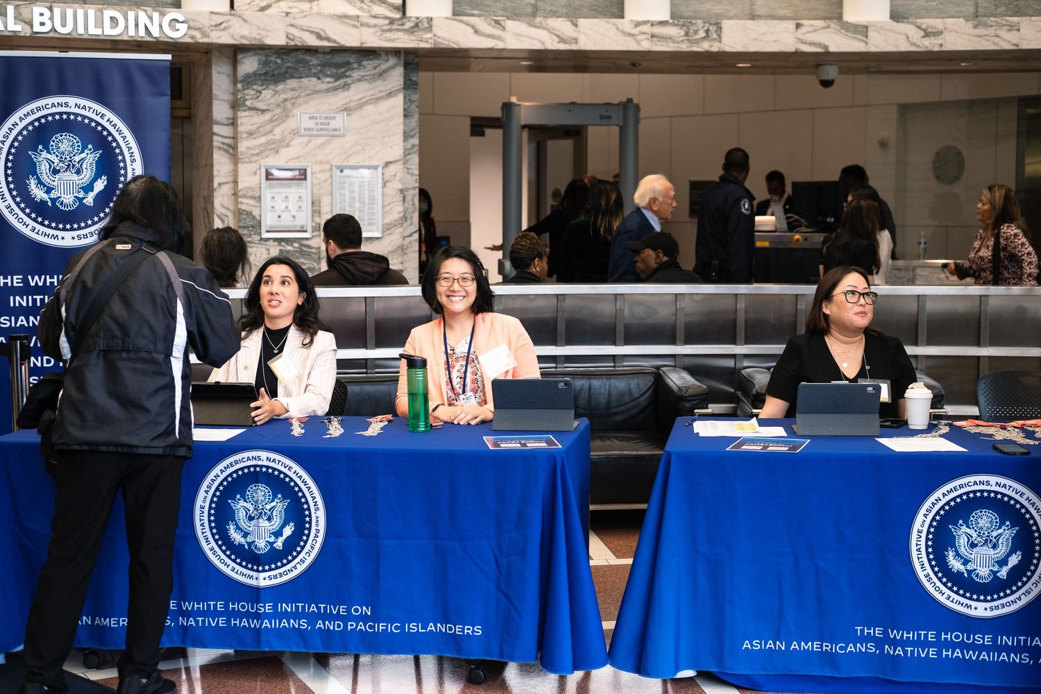 Three women sit at a White House Initiative on Asian Americans and Pacific Islanders registration table in a federal building.