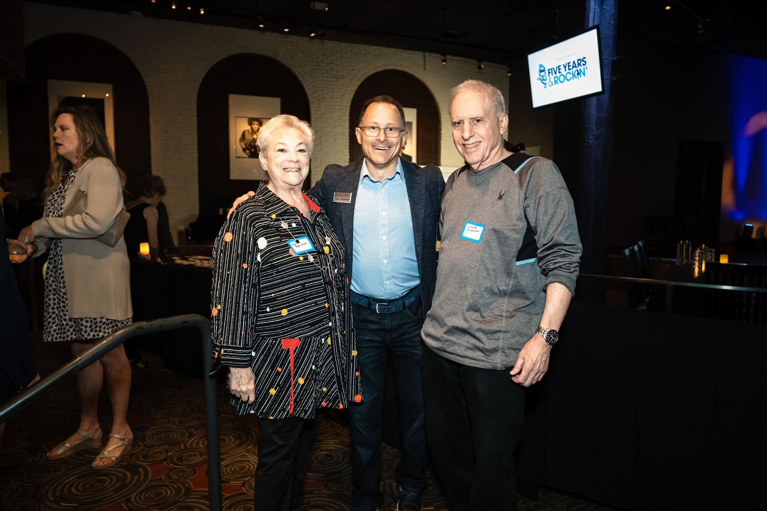 Three smiling attendees pose together at a corporate networking event in a dimly lit venue.