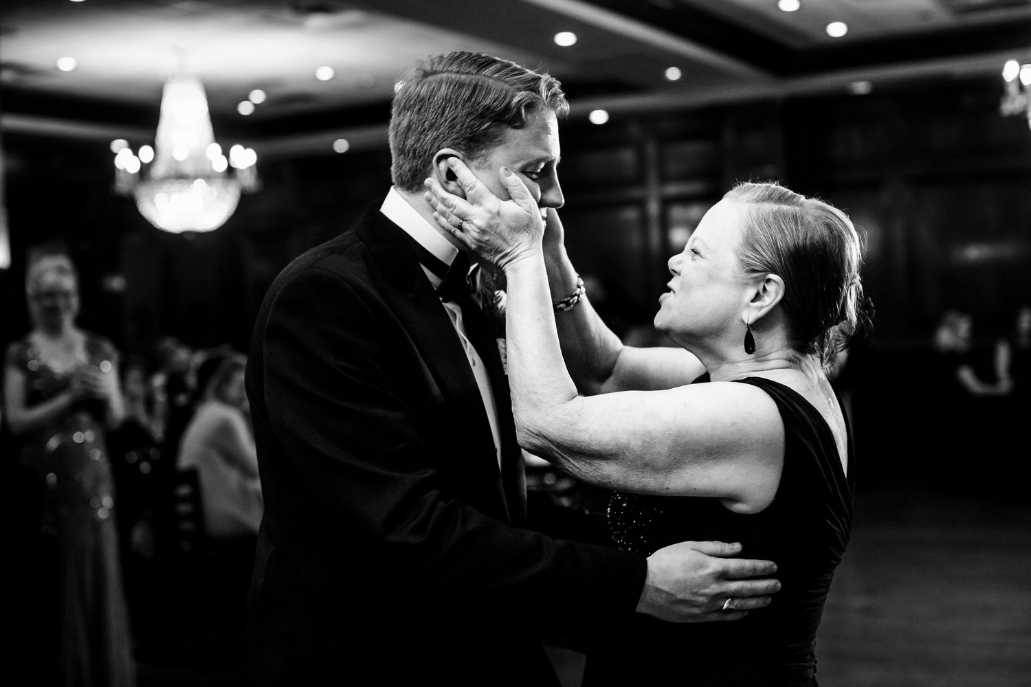 Emotional black and white photo of groom and mother sharing a tender dance at wedding reception.