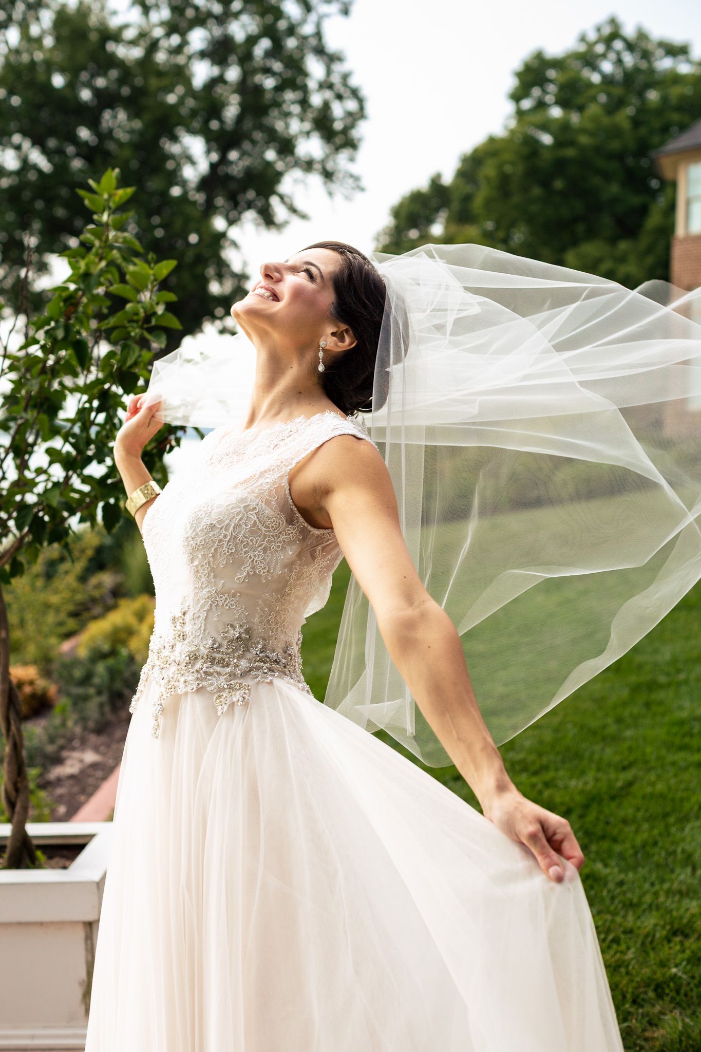 Bride in white lace gown with flowing veil blowing in the wind outdoors.