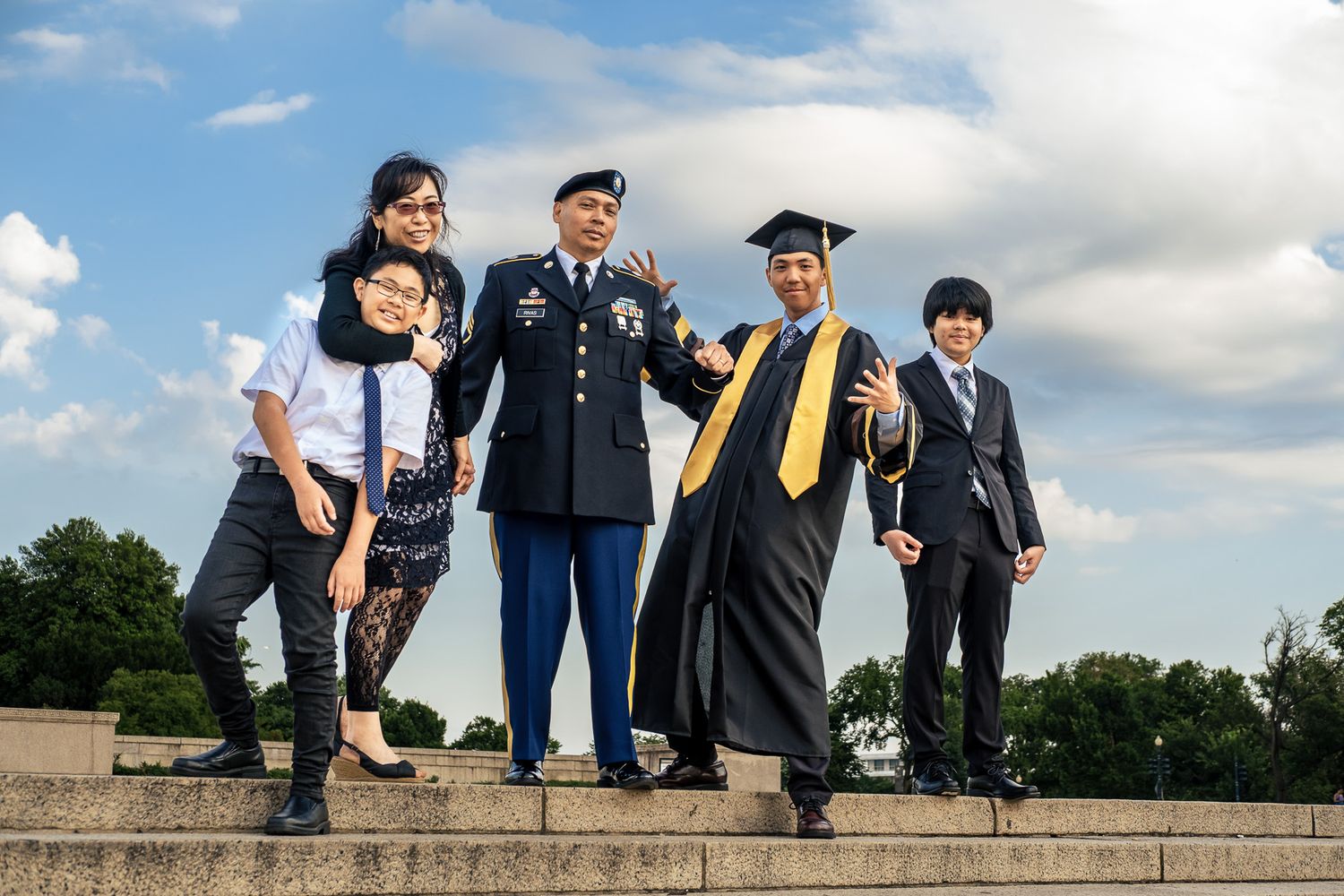 Family of five celebrating graduation outdoors, including military officer and graduate in cap and gown.