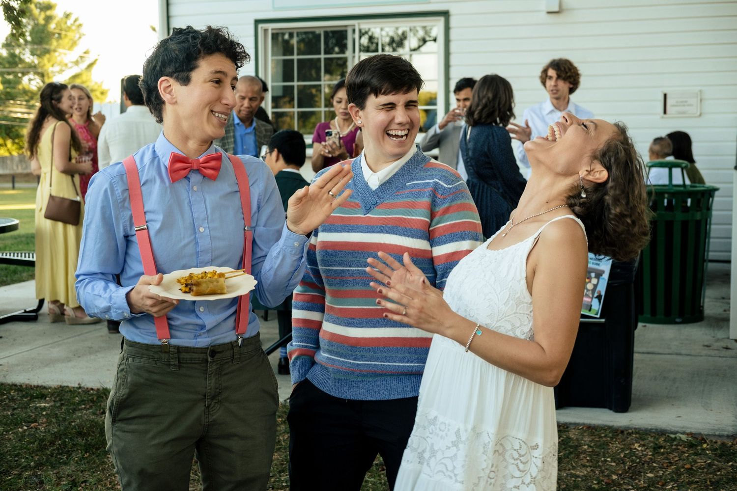 Two young men and a woman laughing together at an outdoor wedding reception celebration.