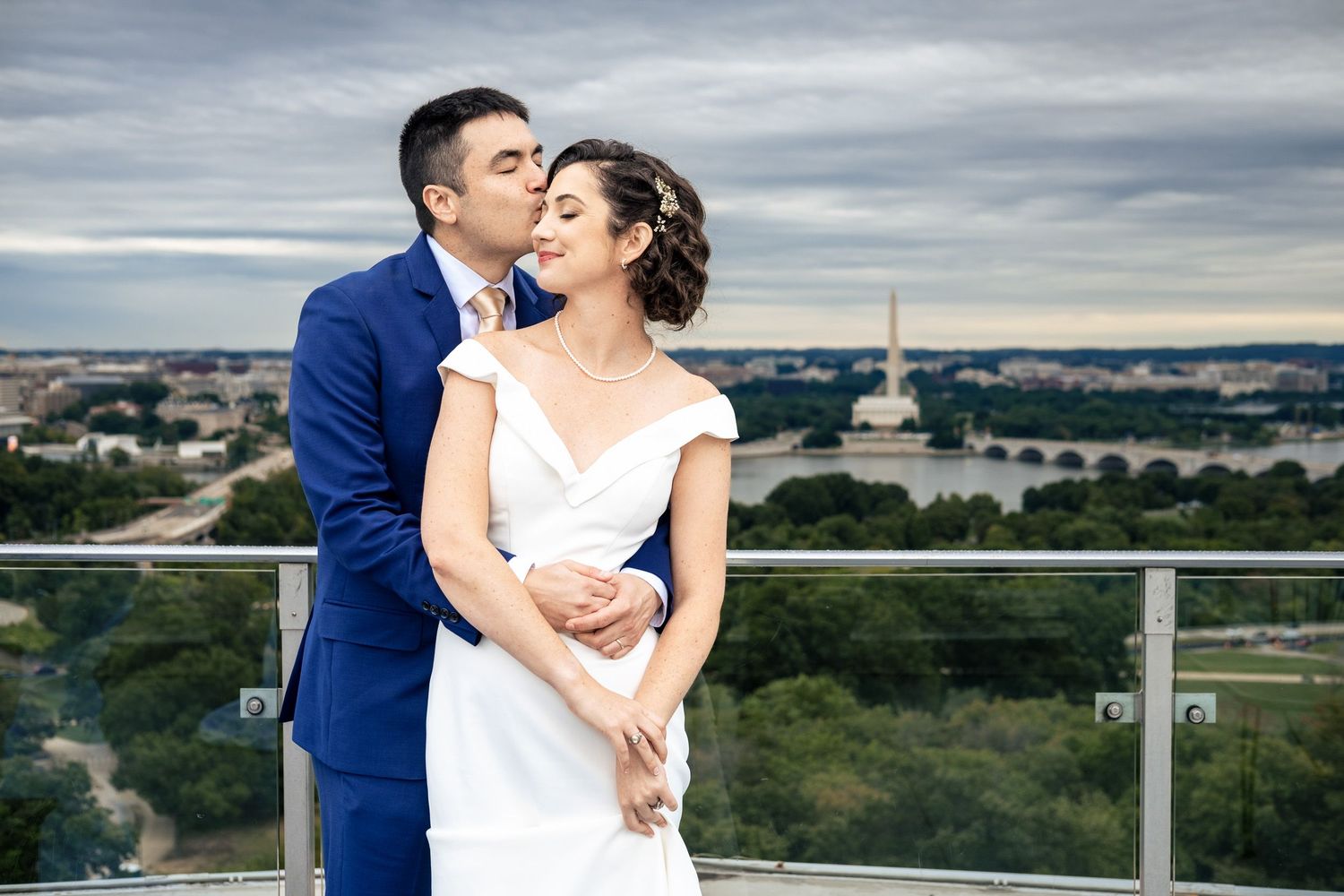 Bride and groom share a romantic kiss on a rooftop with Washington DC skyline in the background.