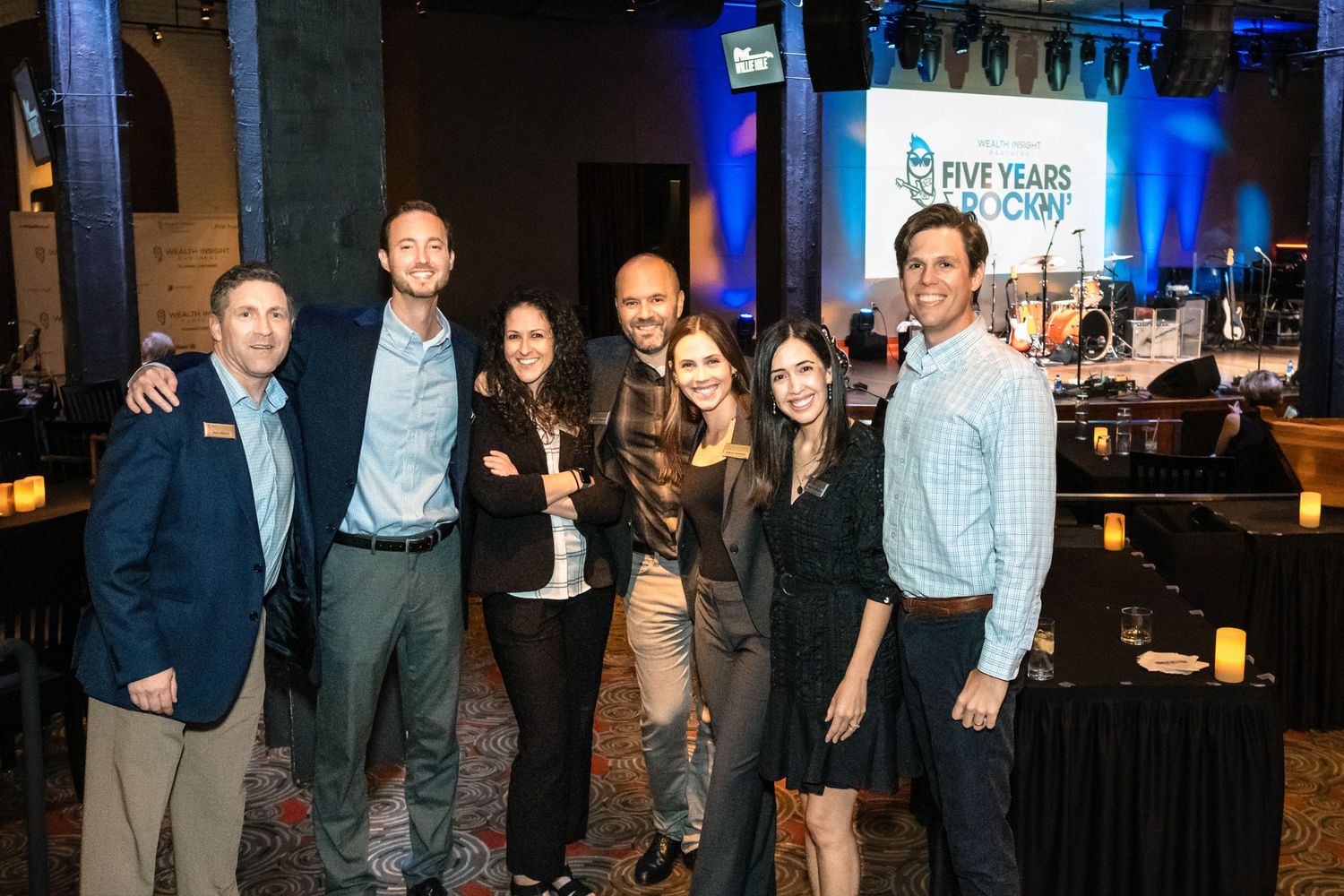 Group of seven professionals smiling at a Five Years Downtown anniversary celebration event in a decorated venue.