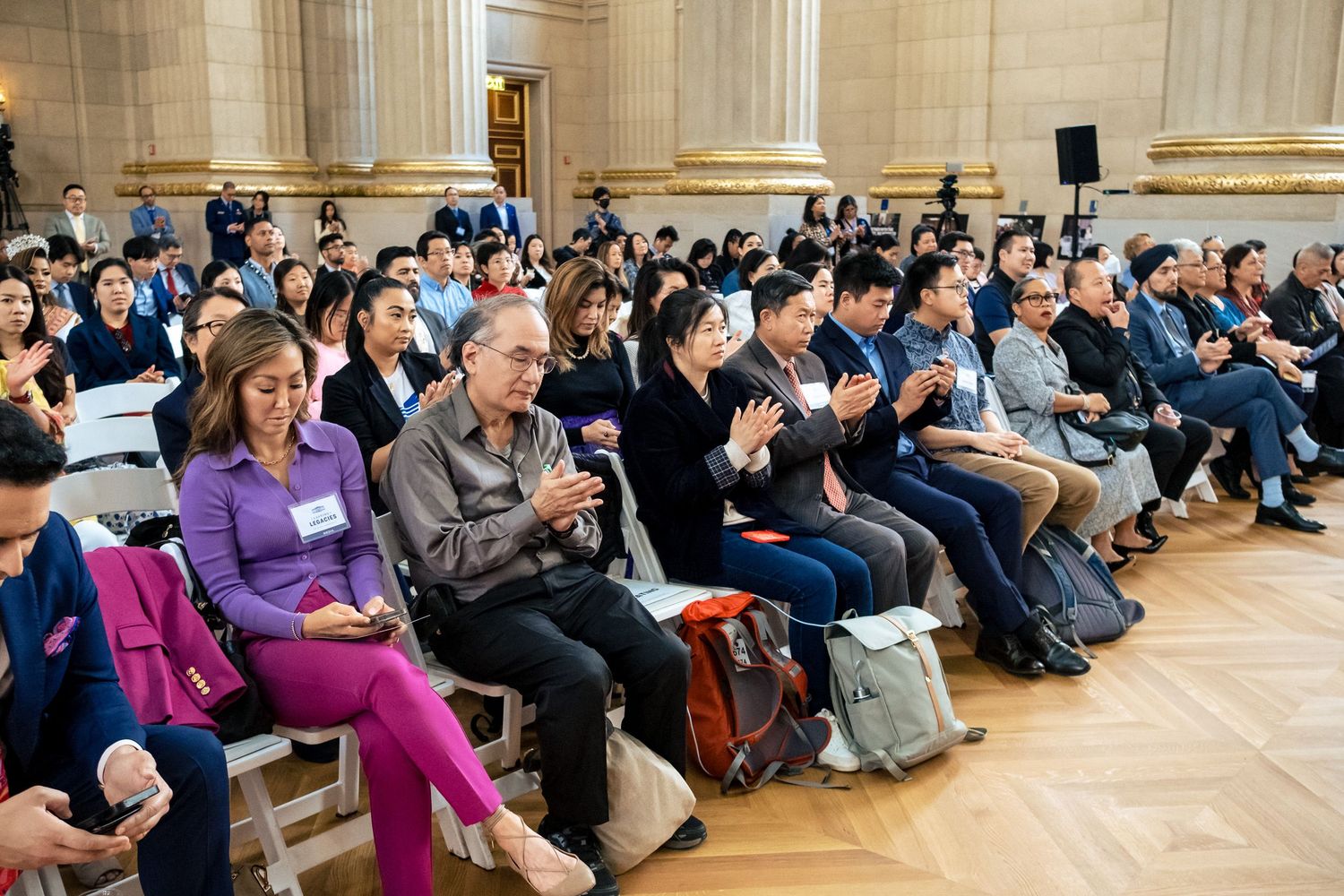 A diverse audience clapping and seated in an elegant hall during a formal event or conference.