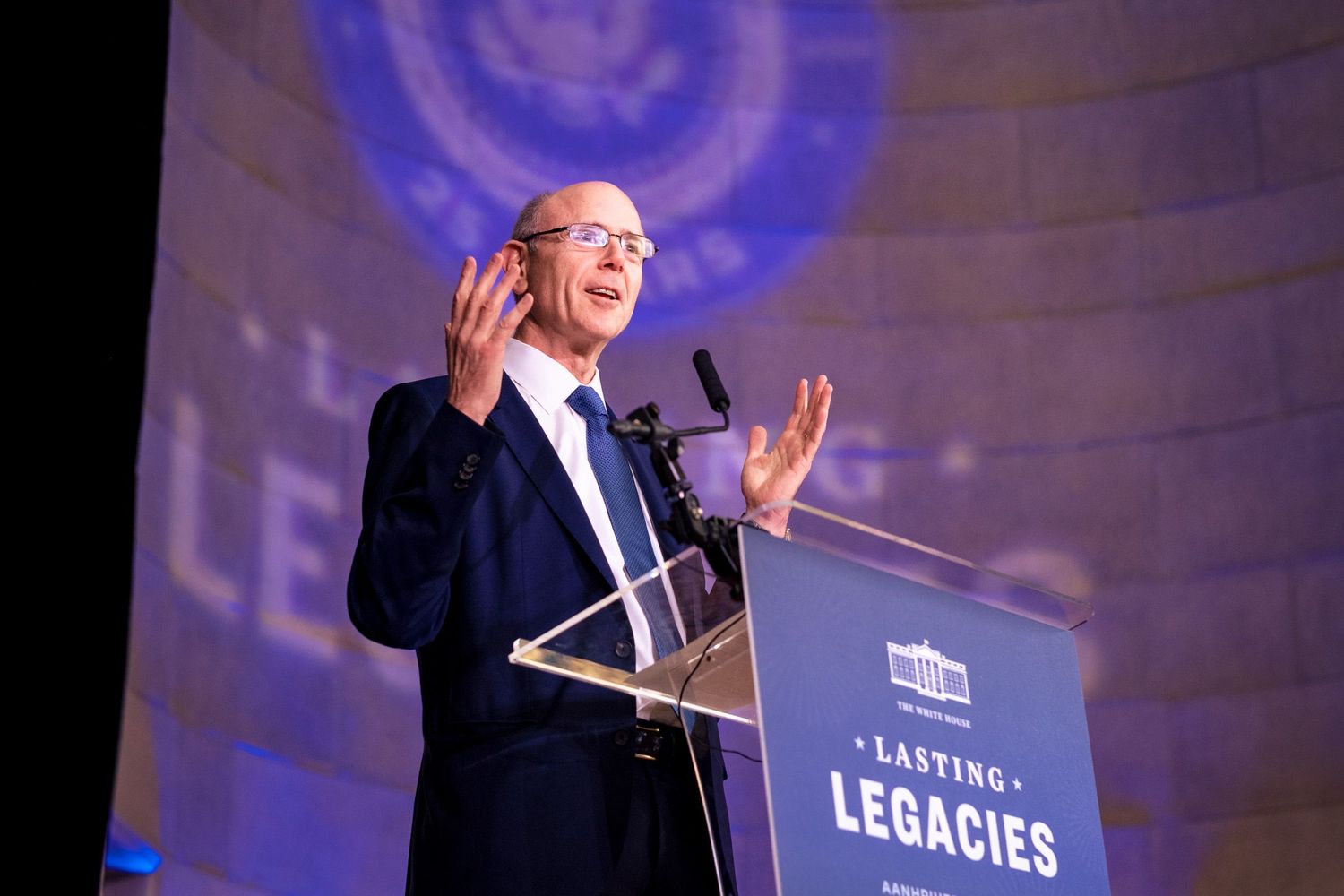 Man speaking at podium during Lasting Legacies event with presidential seal backdrop.