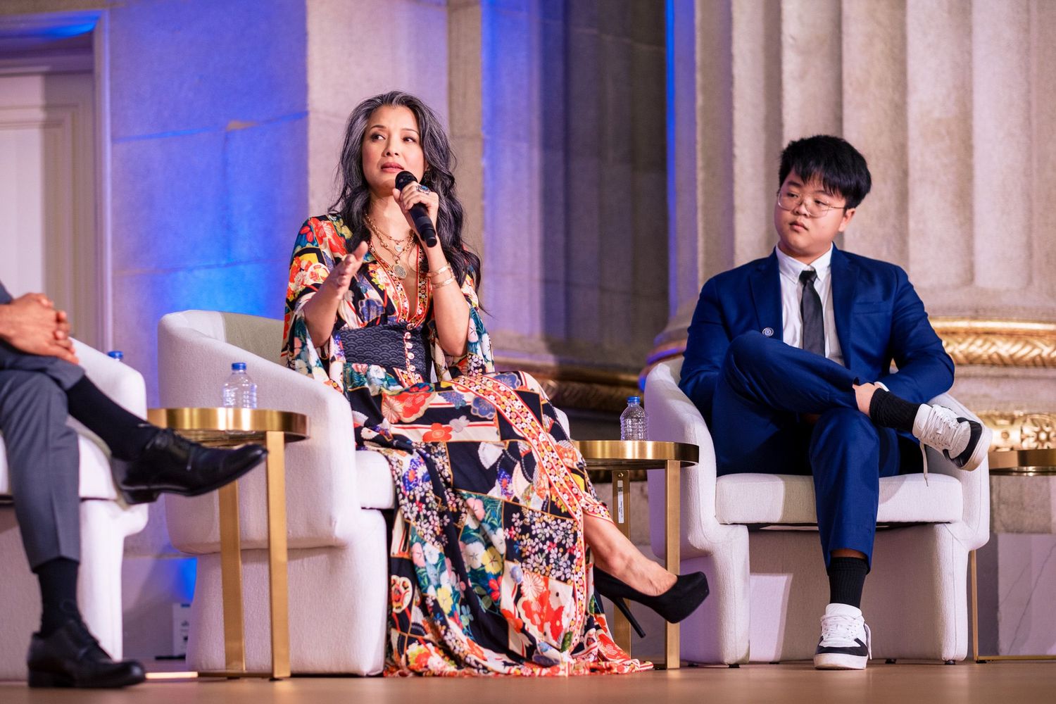 Panel discussion with three speakers seated in white chairs on an elegant stage at a formal event.