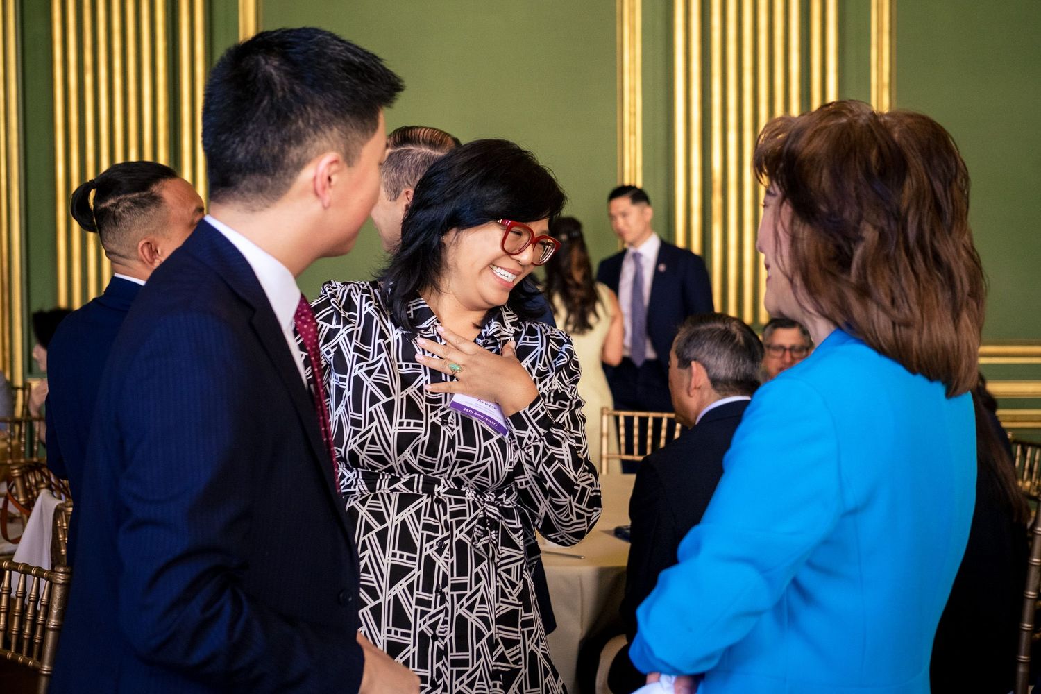 Guests networking at a formal event in an elegant green and gold ballroom during a professional gathering.