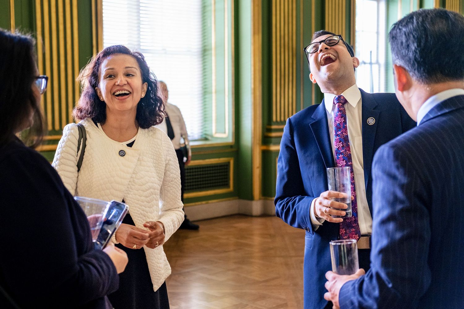 Professionals laughing and socializing at a formal event in an elegant green-walled room.