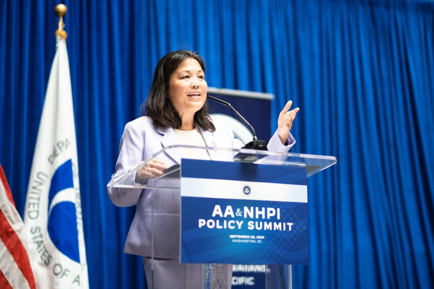 Woman speaking at podium during AA&NHPI Policy Summit with American flag in background.