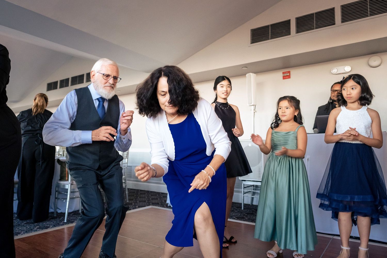 Couple dancing energetically at wedding reception while guests watch and clap.