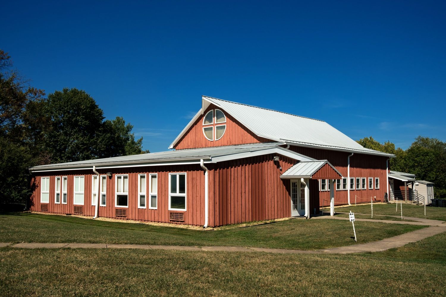 Red barn-style church building with white roof and cross under clear blue sky.
