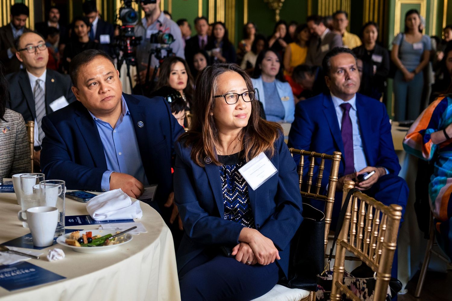 Professionals attend a formal conference event, seated at round tables in an elegant banquet hall.