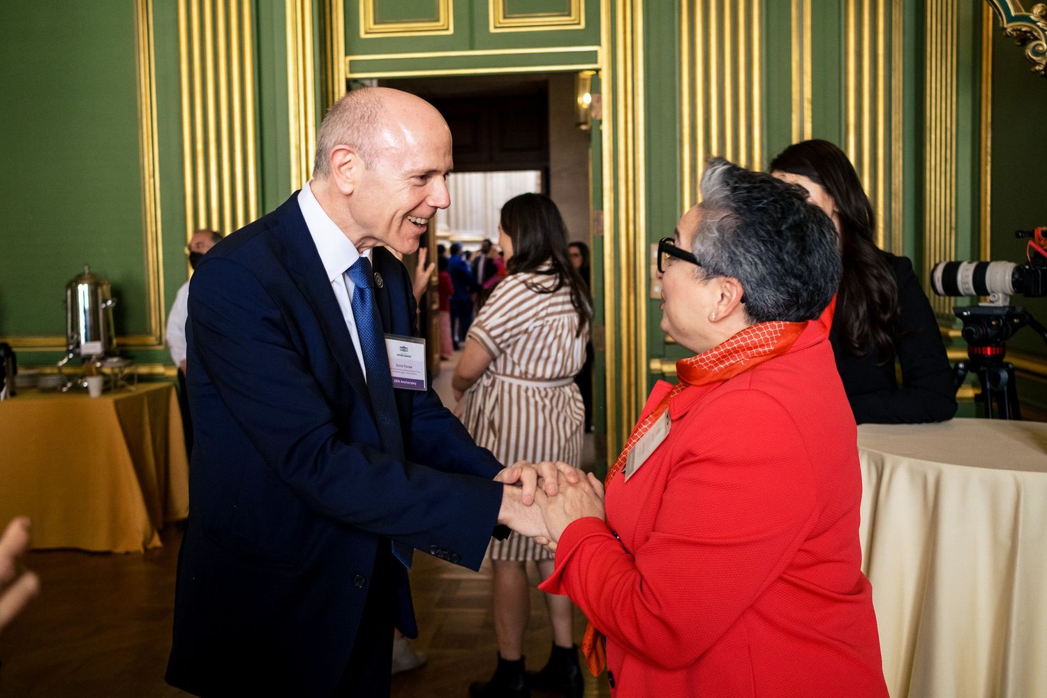 Two professionals shaking hands at a formal networking event in an elegant green-walled venue.