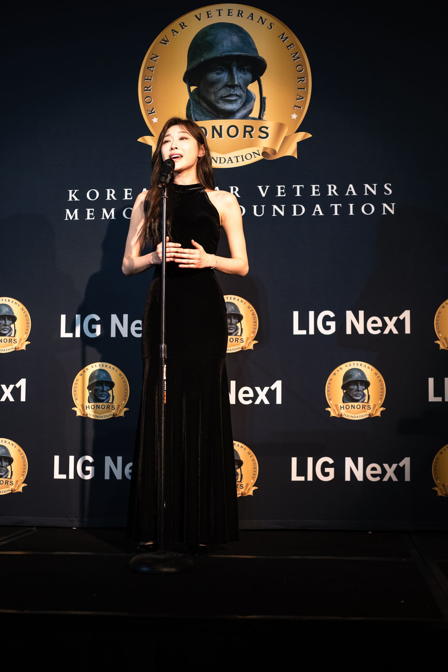 Woman in black gown speaking at microphone at Korean War Veterans Memorial Foundation Honors event.