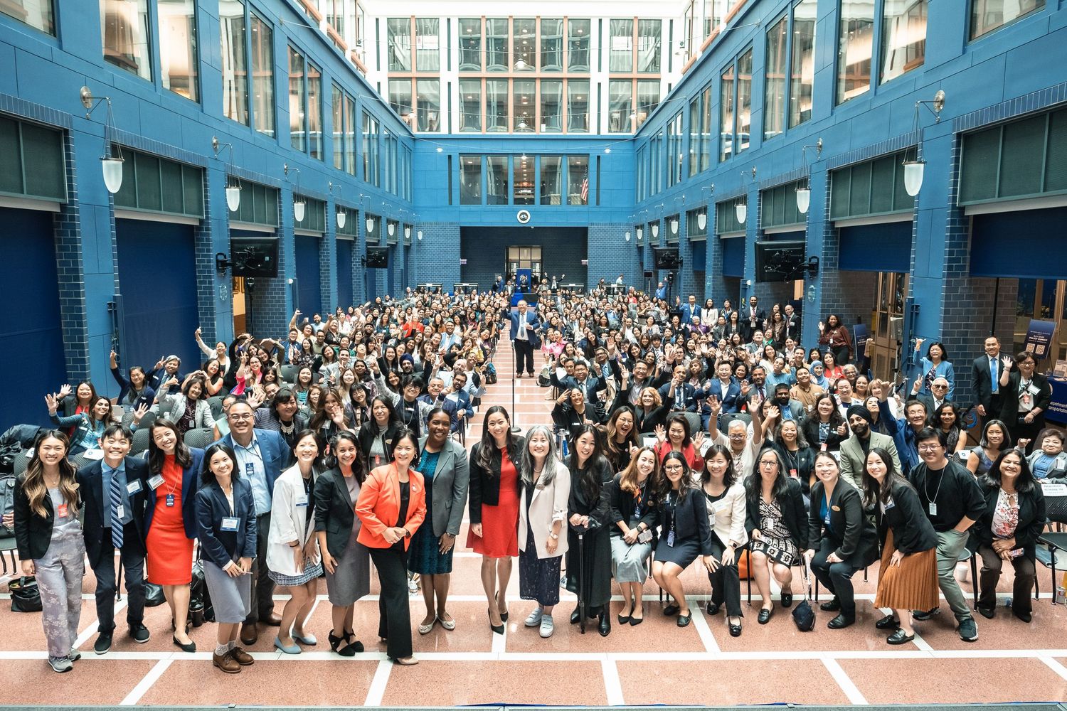 Large group photo of diverse students and faculty gathered in a blue atrium building for a school event.