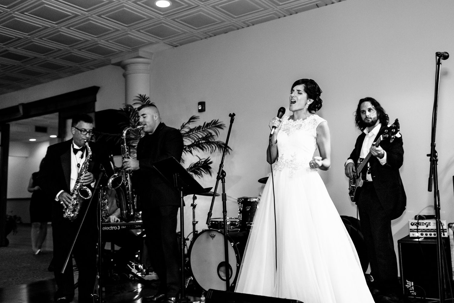 Bride in white gown sings with live band at wedding reception in black and white photo.