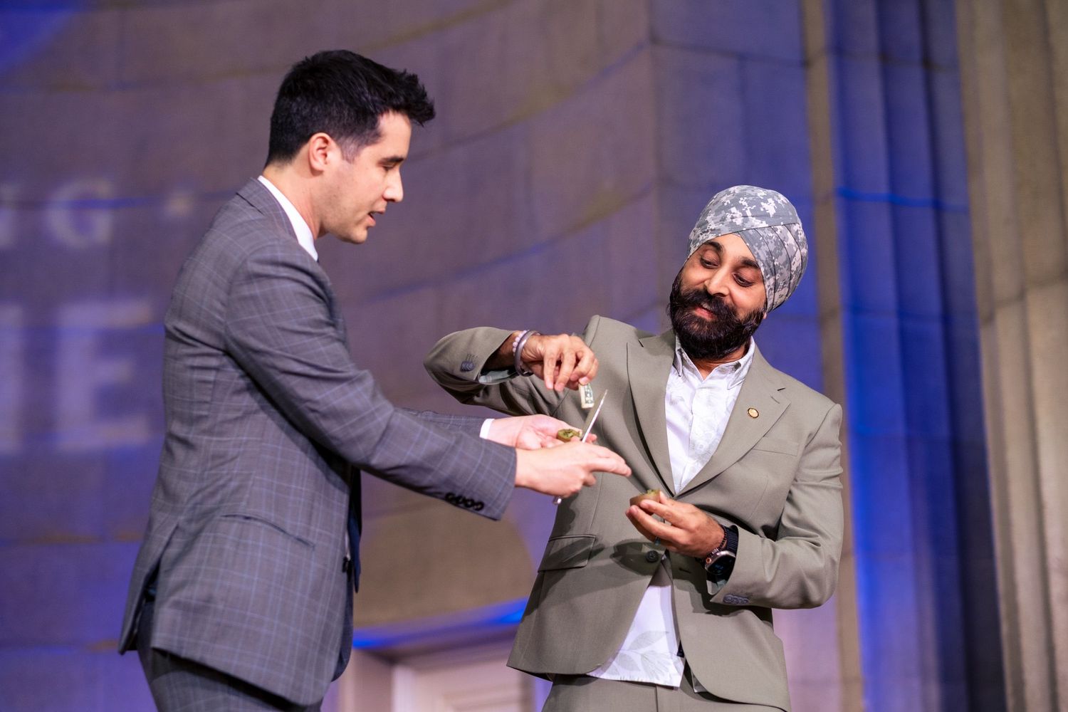 Two men in suits exchange an award on stage at a formal ceremony event.