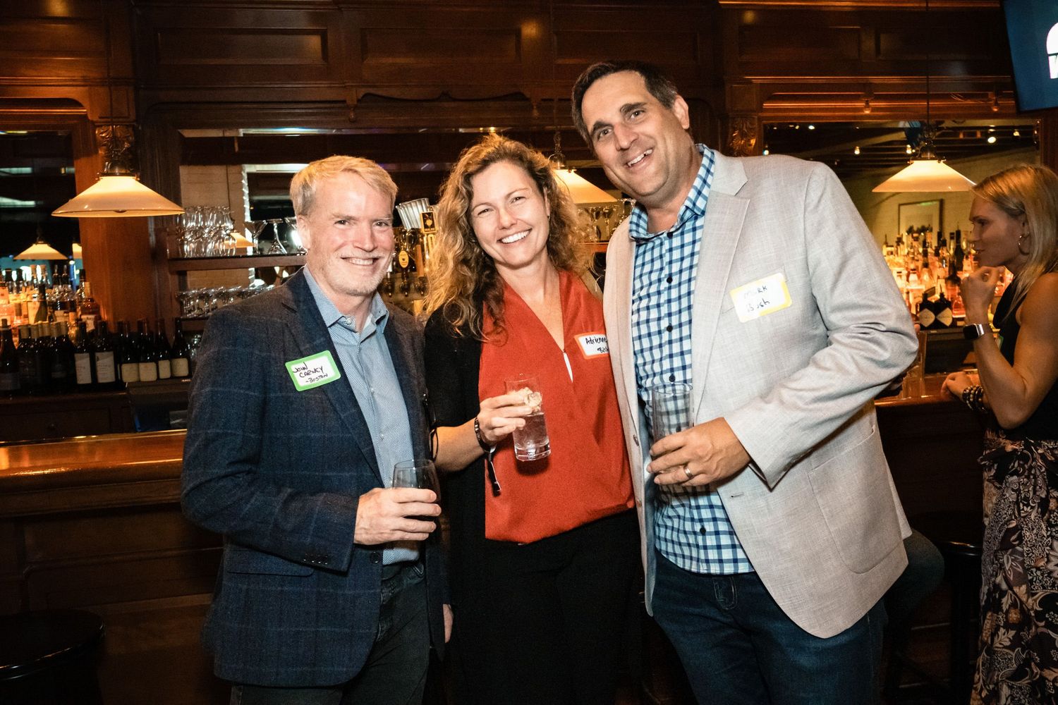 Three people smiling and holding drinks at a casual networking event in a bar.