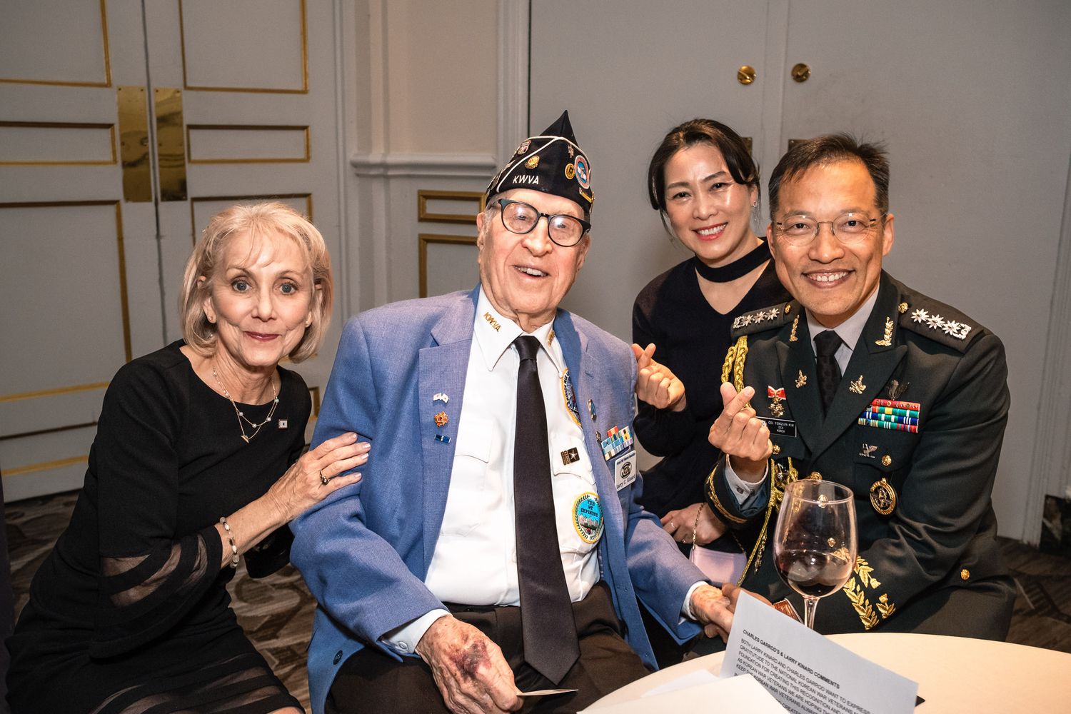 Four people smile together at a formal event, including a veteran in a blue blazer with medals and a military officer.