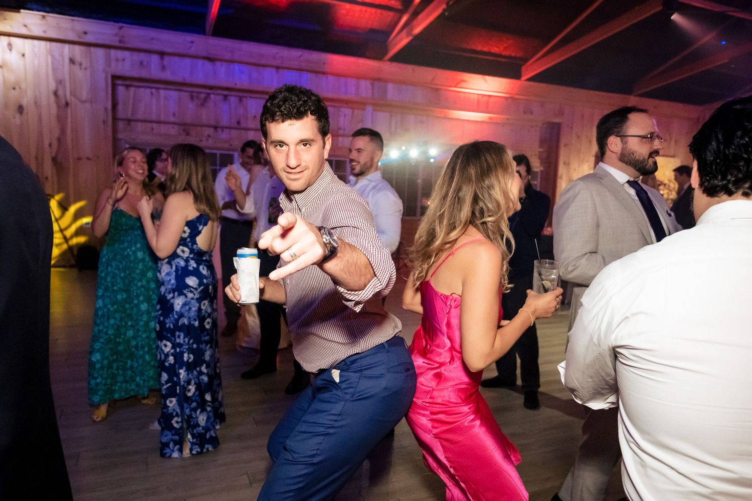 Man dancing energetically at a wedding reception party on a wooden dance floor with colorful lights.