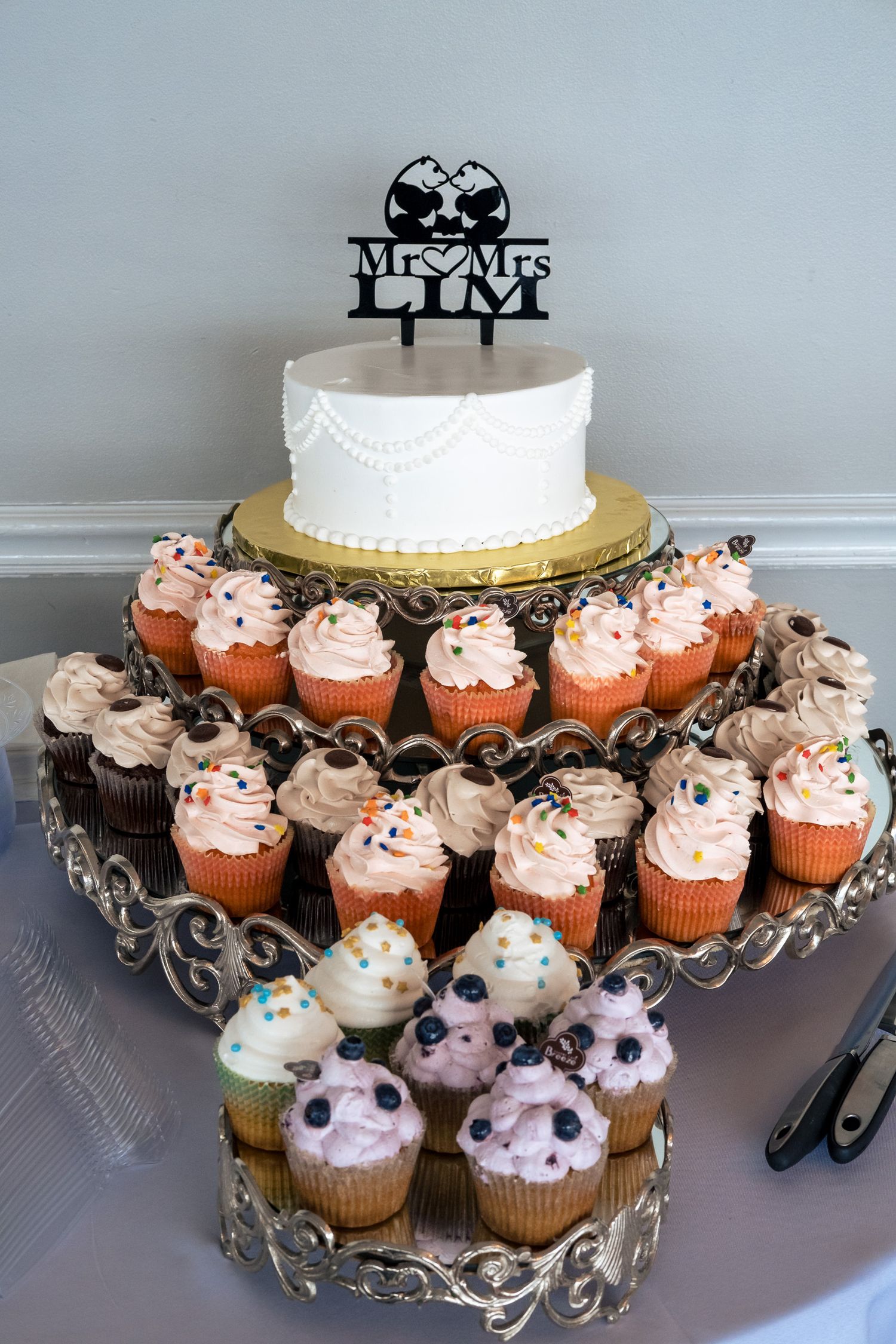 Wedding cupcake tower with Mr. and Mrs. Lim cake topper and white cake surrounded by pink frosted cupcakes.