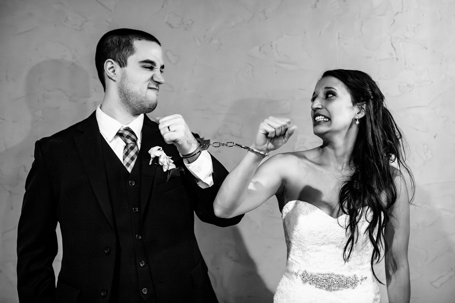 Playful bride and groom pose handcuffed together in a fun black and white wedding portrait.