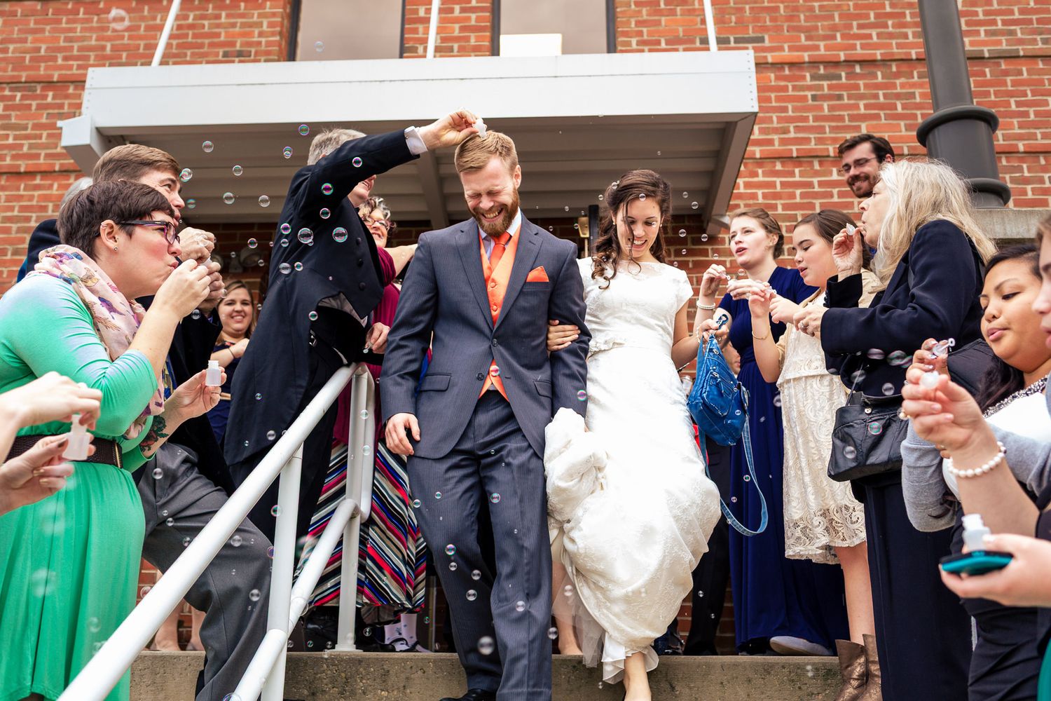 Newlyweds exit church ceremony through bubble send-off surrounded by cheering guests.