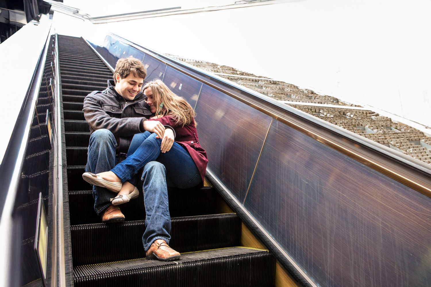 Romantic couple sitting together on escalator steps, sharing a tender moment while riding down.