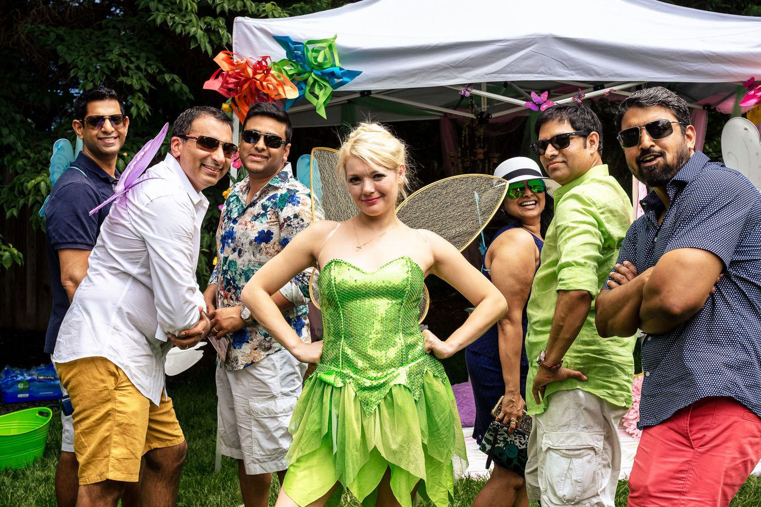 Group of friends posing outdoors with a woman dressed as Tinker Bell in a green costume at a party.