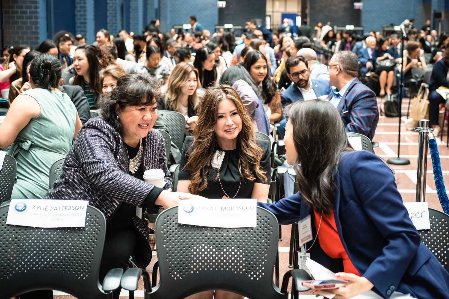 Professionals networking at a conference event, engaged in conversation at tables in a busy venue.