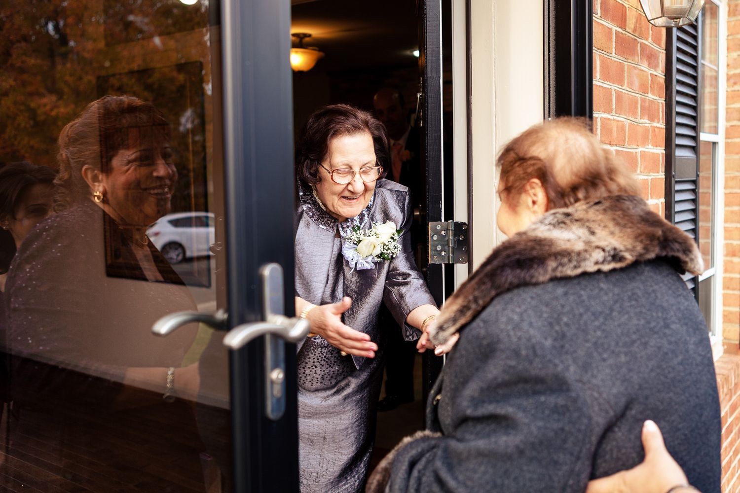 Elderly woman in blue suit greeting guest at wedding venue glass door entrance.