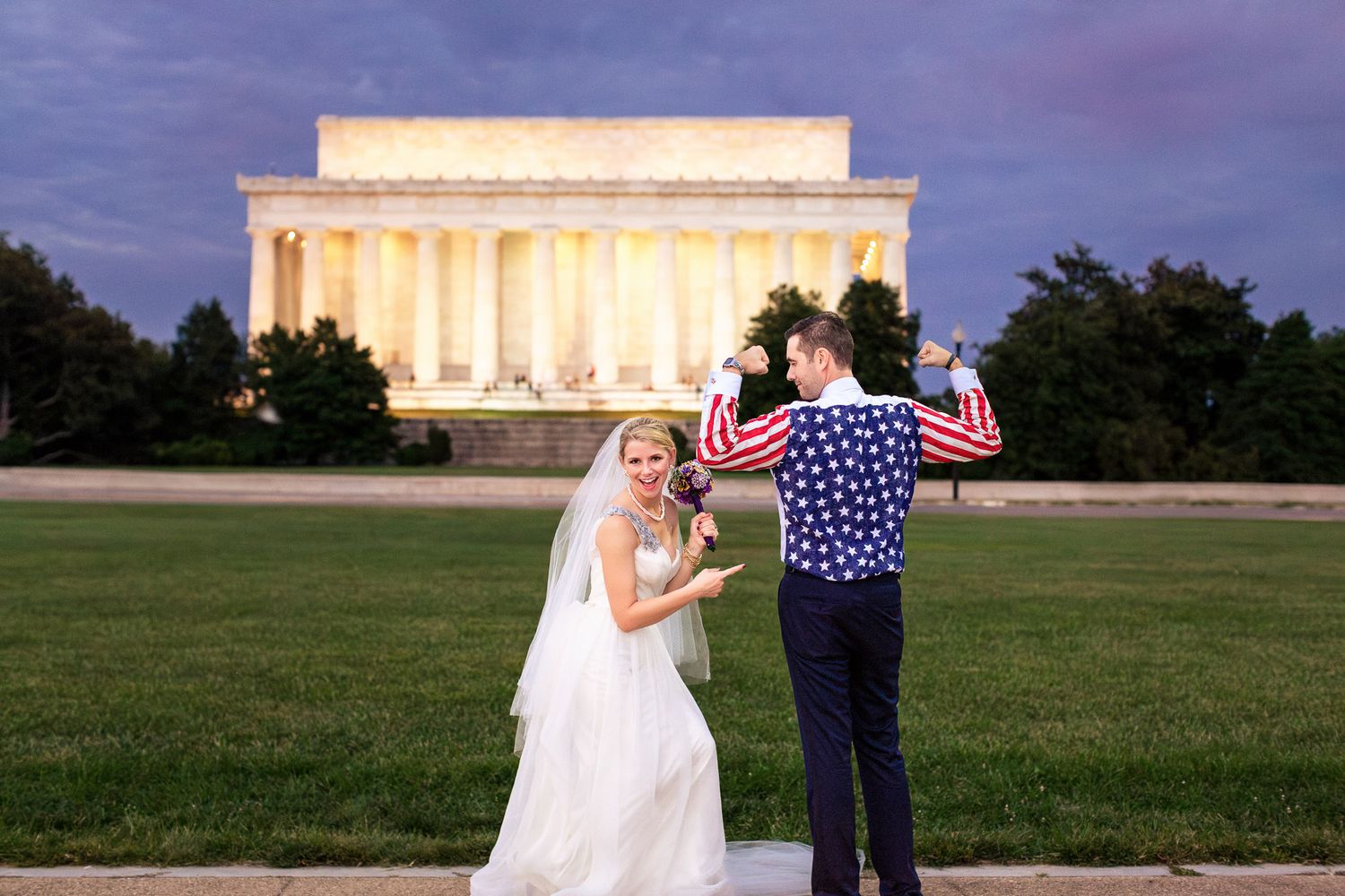 Bride and groom celebrate near the illuminated Lincoln Memorial at dusk with American flag.