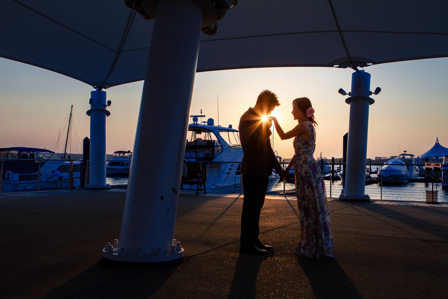 Romantic couple silhouetted against a stunning sunset at a marina during an engagement session.