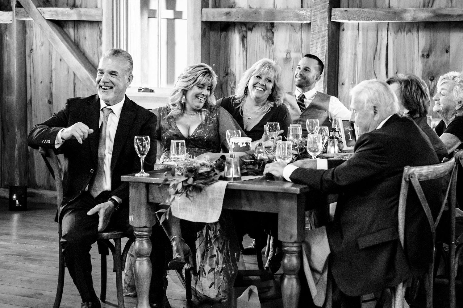 Wedding guests laughing and celebrating together at rustic barn reception dinner table.